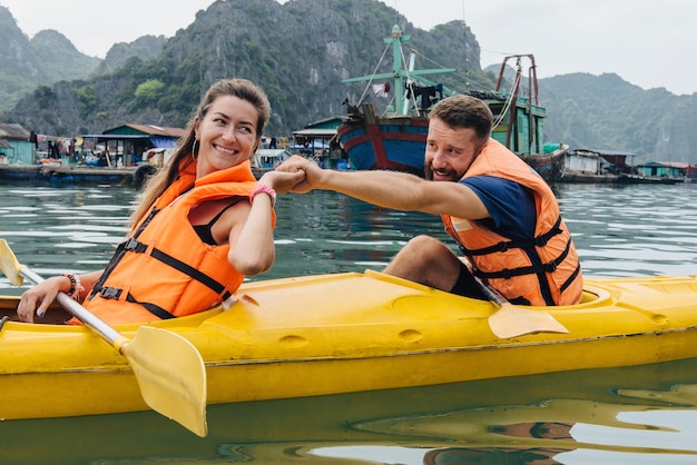 Couple rowing kayak and support each other in Ha Long Bay. Happy people exploring nature.