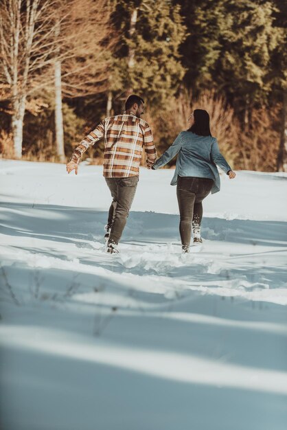 Фото Пара бегает и держится за руки в зимнем заснеженном лесу выборочный фокус