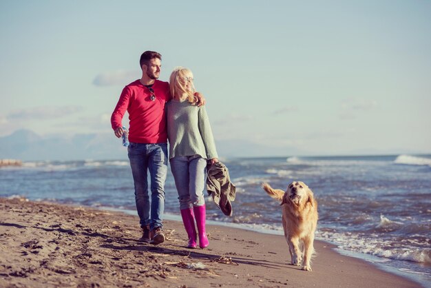 Photo couple running on the beach holding their hands with dog on autmun day