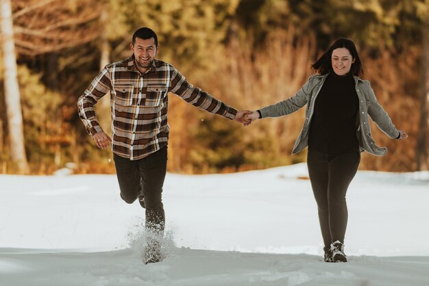 冬の雪に覆われた森で走って手をつないでカップルセレクティブフォーカス