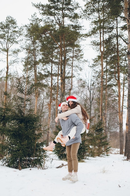 Couple in a Santa hat and hugging and fooling around in a winter coniferous forest