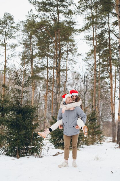 Couple in a Santa hat and hugging and fooling around in a winter coniferous forest