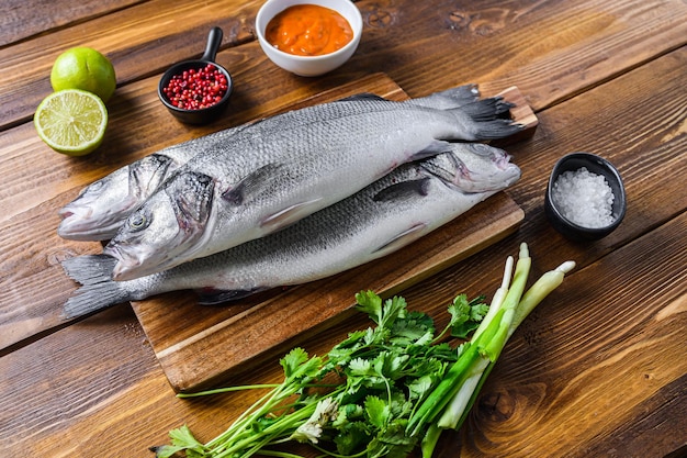 Photo couple sea bass with spices and herbs ingredients overwood table side view