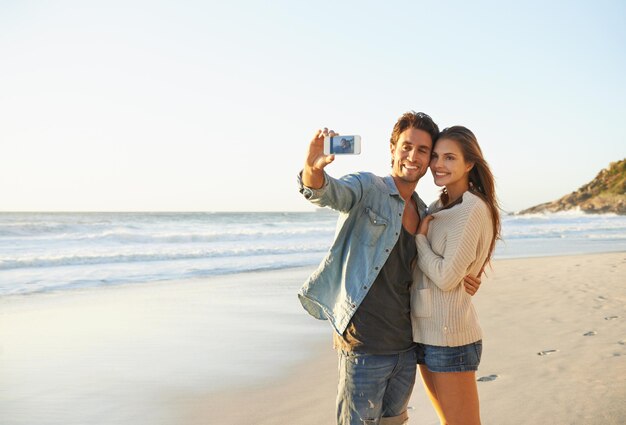 Couple selfie and happy for hug by sea for memory on vacation with care love and mock up space Man woman and smartphone for photography profile picture and mobile app at beach on social media