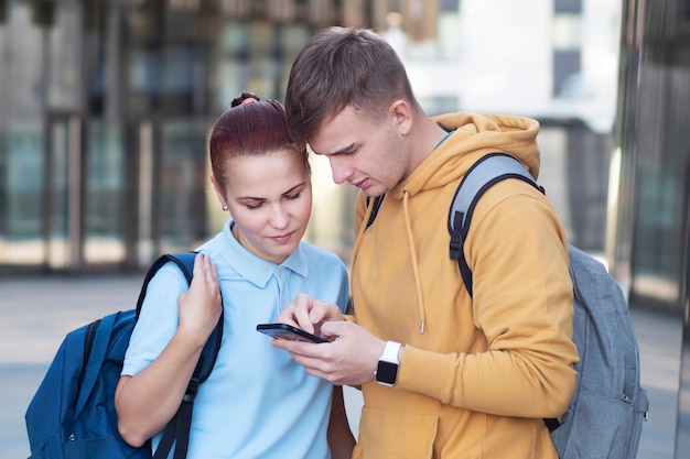 Couple, serious guy and girl looking attentively at cell mobile phone, boy is serfing, browsing at his smartphone