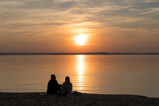 Couple on the shore of the lake during summer sunset and beautiful evening sky romance love