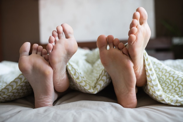 Photo couple showing their feet while lying on a bed