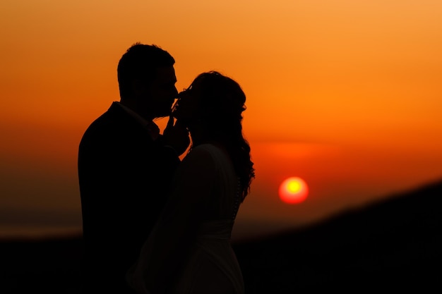 A couple in silhouette with the sun setting behind them