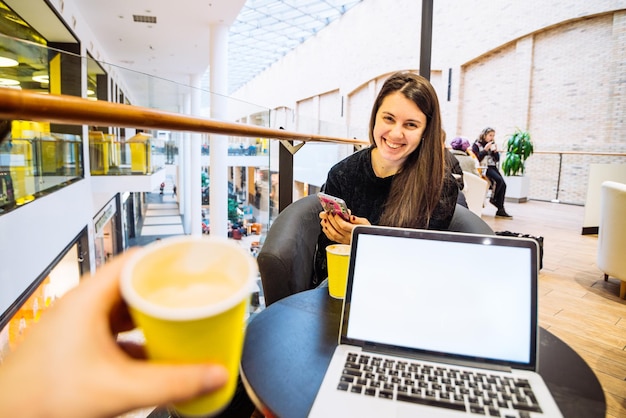 Couple sit in cafe drink coffee in yellow cups man working on laptop while woman check her phone copy space