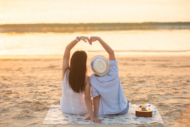 couple sit on sand looking sunset in sea together.