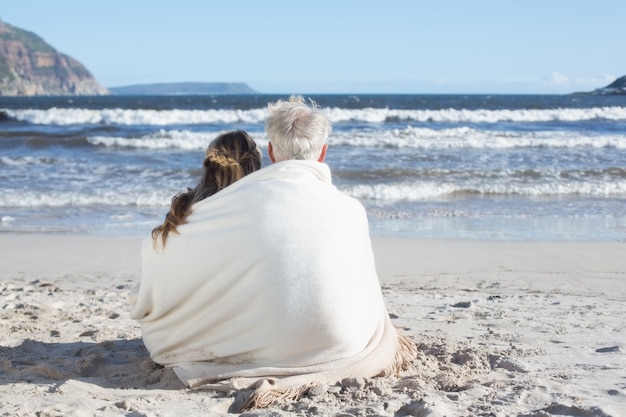 Couple sitting on the beach under blanket looking out to sea