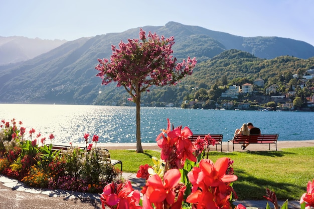 Пара сидит на скамейке на набережной дорогого курорта в Асконе на озере Маджоре, кантон Тичино, Швейцария.