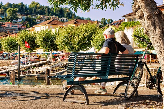 Couple sitting on the bench at the promenade of the luxurious resort in Ascona on Lake Maggiore of Ticino canton in Switzerland.