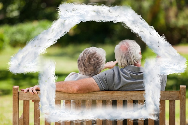 Couple sitting on the bench with their back to the camera against house outline in clouds