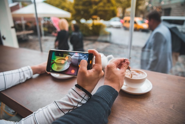 寒い秋の日に暖かいお茶を飲むカフェに座っているカップル instagram の電話で写真を撮る女性
