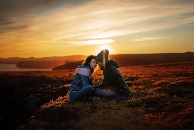 Photo couple sitting on field against sky during sunset