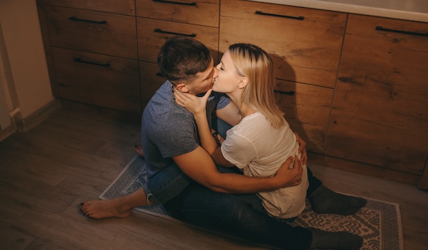 Photo couple sitting on floor in the kitchen and kissing each other while hugging sweetly