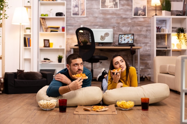 Couple sitting on the floor and watching TV in their living room.