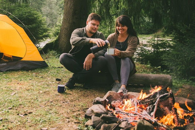 火のそばに座って、熱いお茶のハイキングの概念を飲むカップル