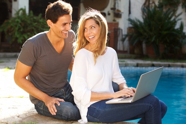 Couple sitting outside together by pool with laptop