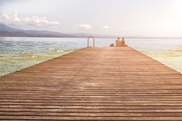 桟橋のぶら下がっている足に座っているカップルは、湖に沈む夕日を観察しました