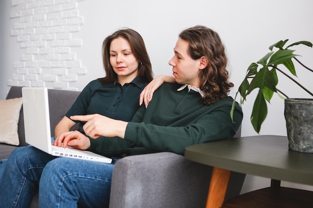 Couple sitting on the sofa with notebook and phone Man and woman communicating on the laptop phone