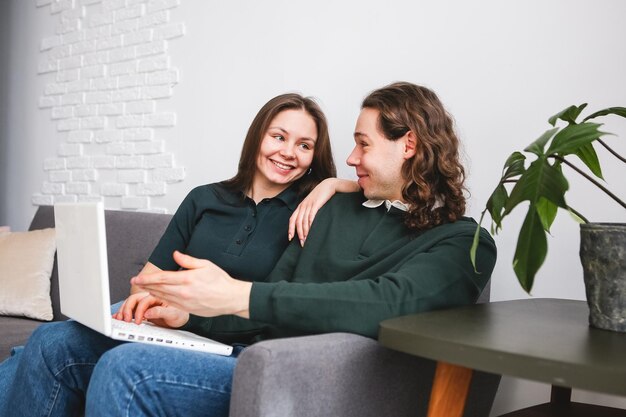 Couple sitting on the sofa with notebook and phone Man and woman communicating on the laptop phone