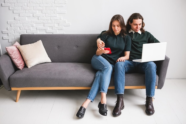 Photo couple sitting on the sofa with notebook and phone man and woman communicating on the laptop phone