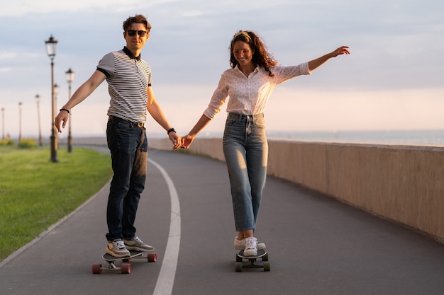 Couple of skateboarder ride longboard holding hands happy young adults enjoy longboarding on sunset