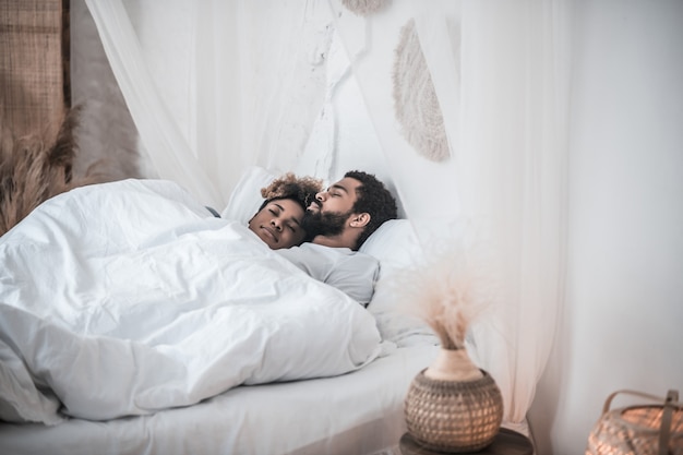 Couple, sleep. young adult dark skinned man and woman sleeping together in bedroom under blanket