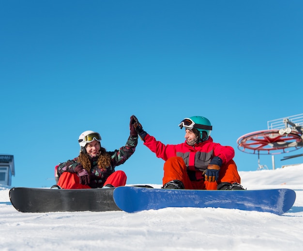 スノーボーダーのカップルが雪の上に座っている間お互いにハイファイブを与える