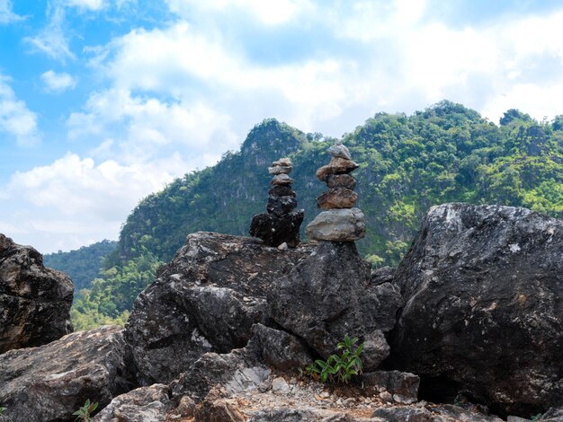 Couple of stacking stones or pebbles on big rough rock with green mountain view and cloudy bright blue sky in the background. peaceful and tranquil nature. mine stone.