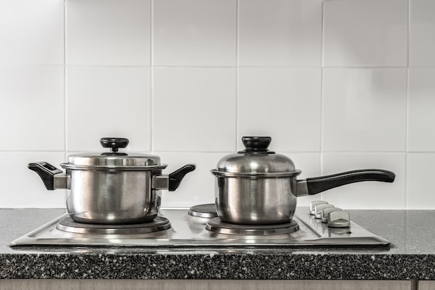 Photo couple of stainless pots on kitchen stove with marble counter top and white tile wall
