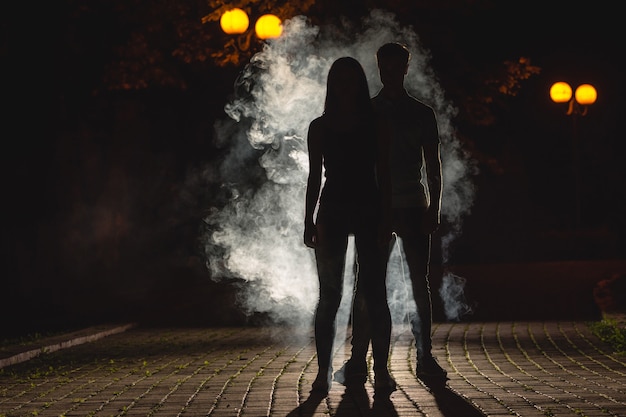 The couple stand on the dark alley on the fume background. night time