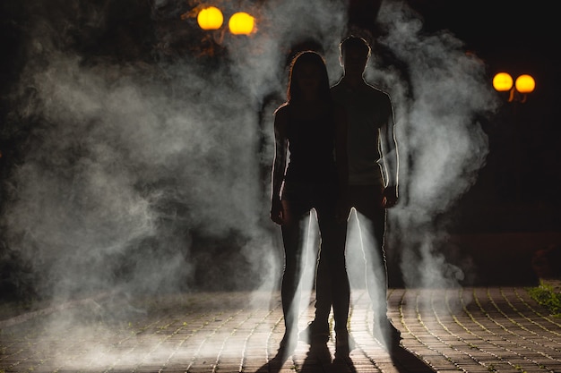 The couple stand on the dark alley on the fume background. night time