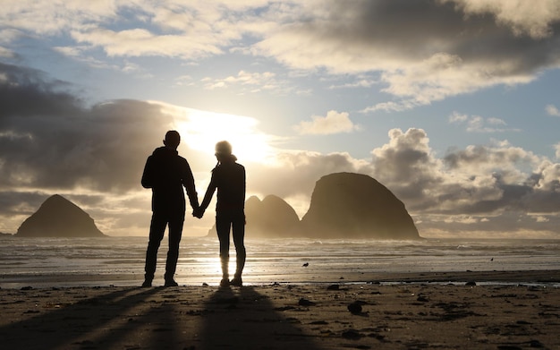 couple standing on beach against sky during sunset