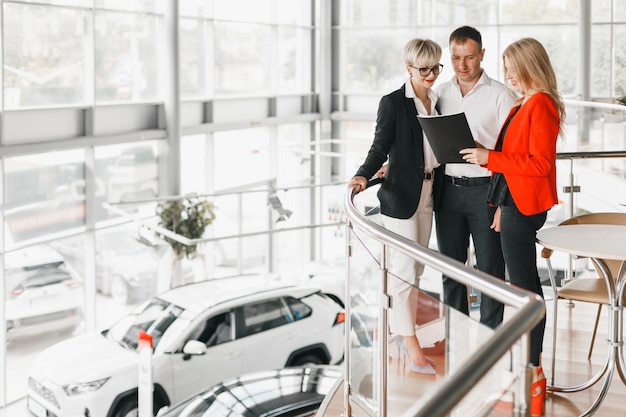 Couple standing hugging in interior of dealership with dealer.