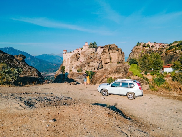 Couple standing near car looking at meteora monastery Thessaly mountains Greece