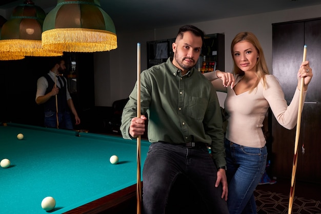 Couple standing near the pool billiard table, they posing after game. leisure time