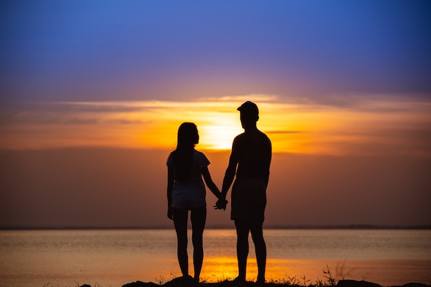 The couple standing near a water on the sunset background