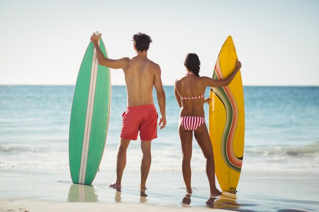 Couple standing with surfboard on beach