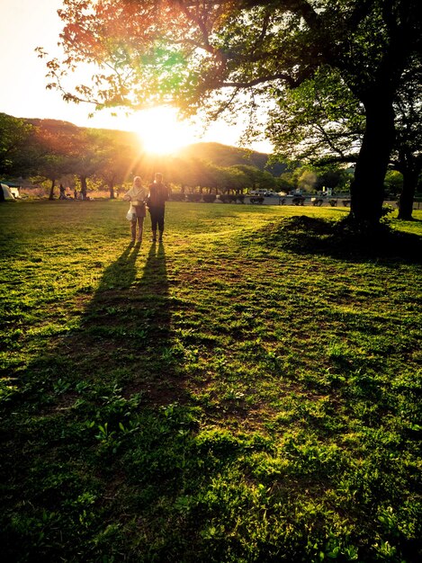 A couple stands in a field with the sun shining on them