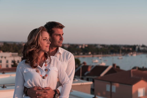 a couple stands on a rooftop overlooking the water