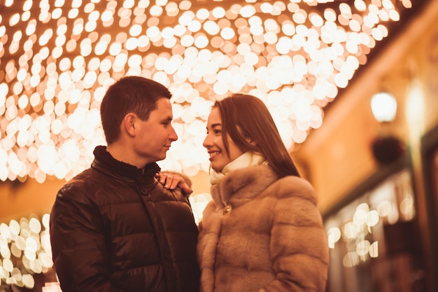 Coppia in strada prima del periodo natalizio. sfondo di decorazioni con luci bokeh