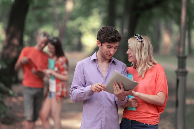 公園に立っている試験の質問を議論するクリップボードを持つ学生のカップル