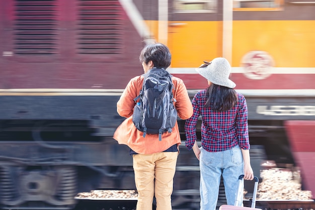 Couple of stylish tourists with backpacks and going into train at outdoor metro station, Asian couple traveling train station vintage style concept, in thailand