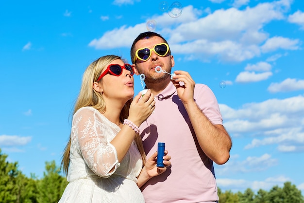 Photo couple in sunglasses blowing soap bubbles summer against a blue