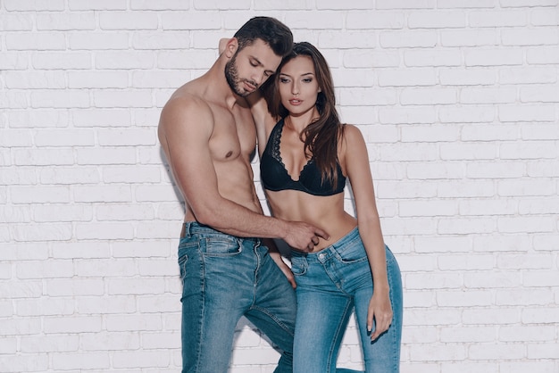 Couple in syle. Beautiful young couple embracing while standing against brick wall