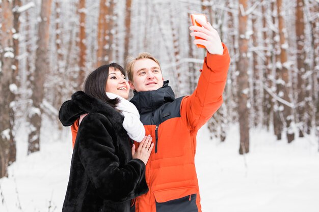 Couple taking self portrait with smart phone in winter park. Beautiful young couple selfie.