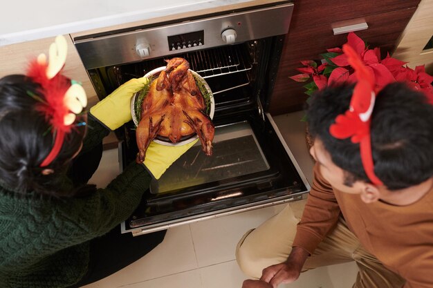 Couple taking tray with turkey out of oven view from above